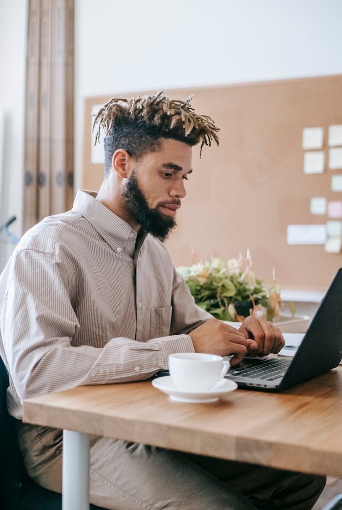 Adult man concentrating on laptop work in a home office setting with coffee and notes.